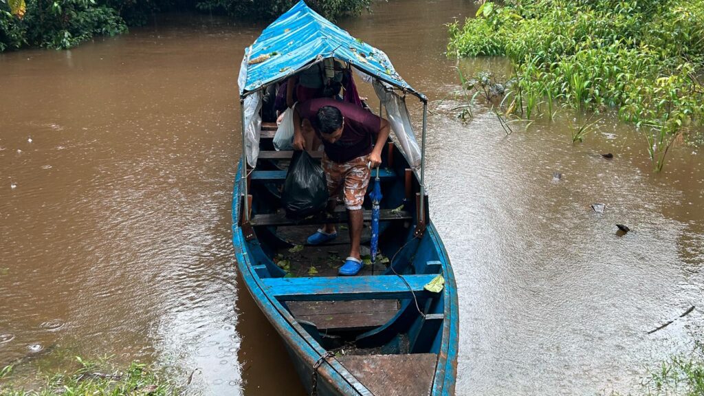 Man steps off a blue wooden boat onto the jungle shore during rain near Iquitos, Peru