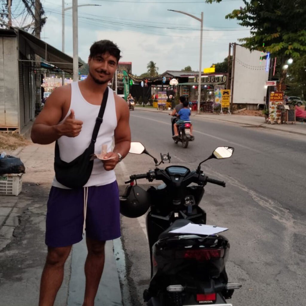 Smiling man with motorbike giving a thumbs up on a street in Koh Samui, Thailand — embracing local life as a digital nomad during low season