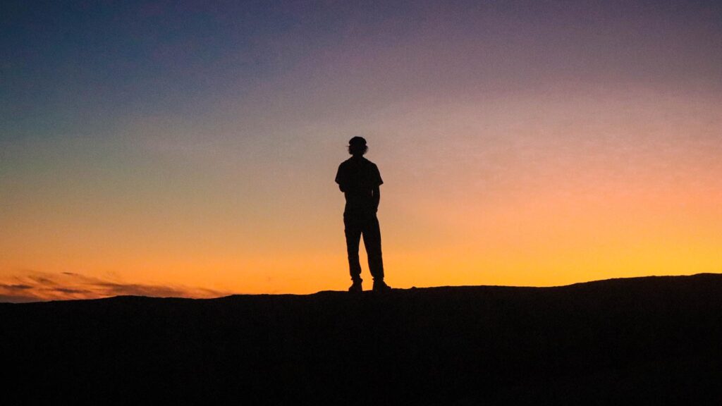 Silhouette of a man standing on a ridge at sunset, symbolizing reflection, freedom, and the solitude of digital nomad life
