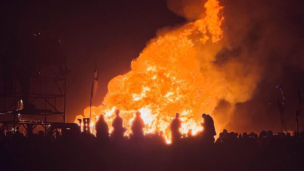 Crowd watches the iconic main burn at AfrikaBurn as flames rise into the night sky — symbolizing transformation and release
