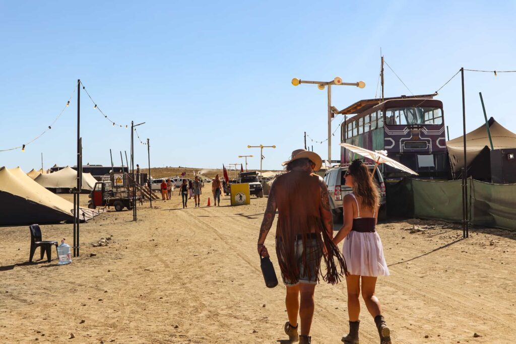 Festivalgoers walk hand-in-hand past themed camps and art cars at AfrikaBurn, capturing the sense of freedom and desert community life